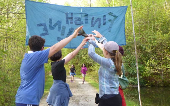 In the background, two students run forward toward a banner that appears to read "finish line." In font of the banner, four people make an archway with their lifted arms.
